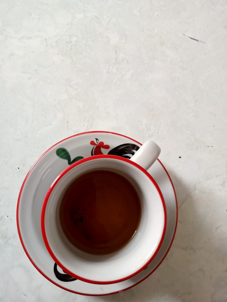 A white and red teacup with tea in it as seen from above.