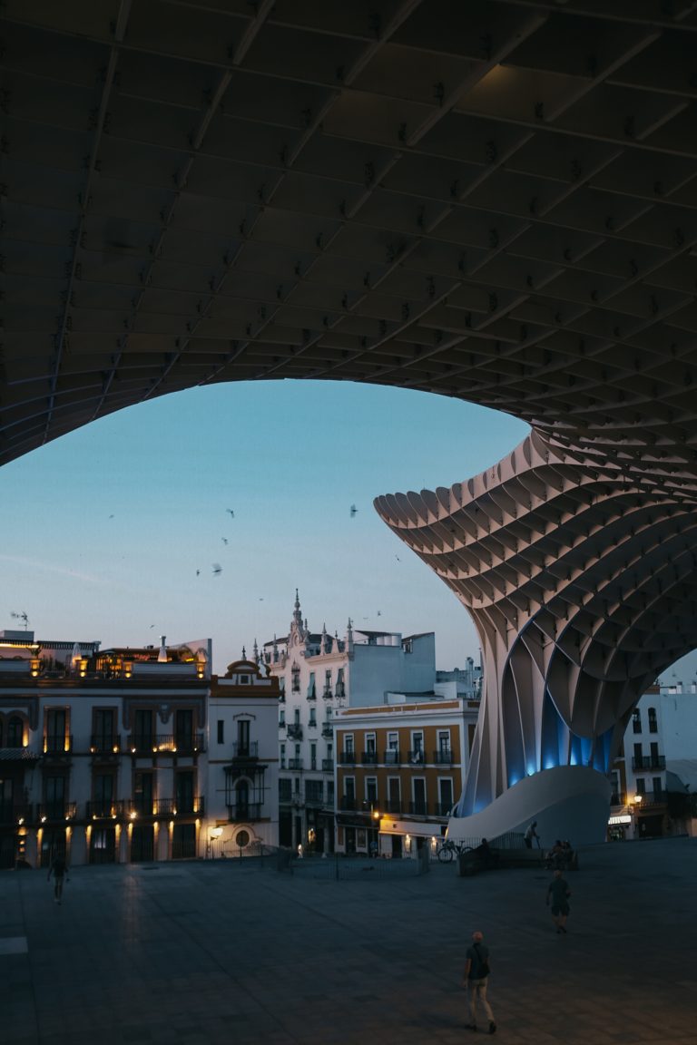 View of Setas de Sevilla in Spain looking out over the city at dusk with birds flying in the air and people milling about.