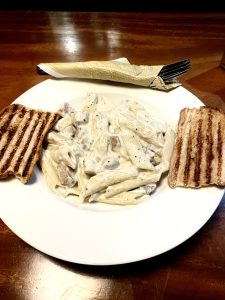 White sauce chicken pasta served with two pieces of garlic bread.