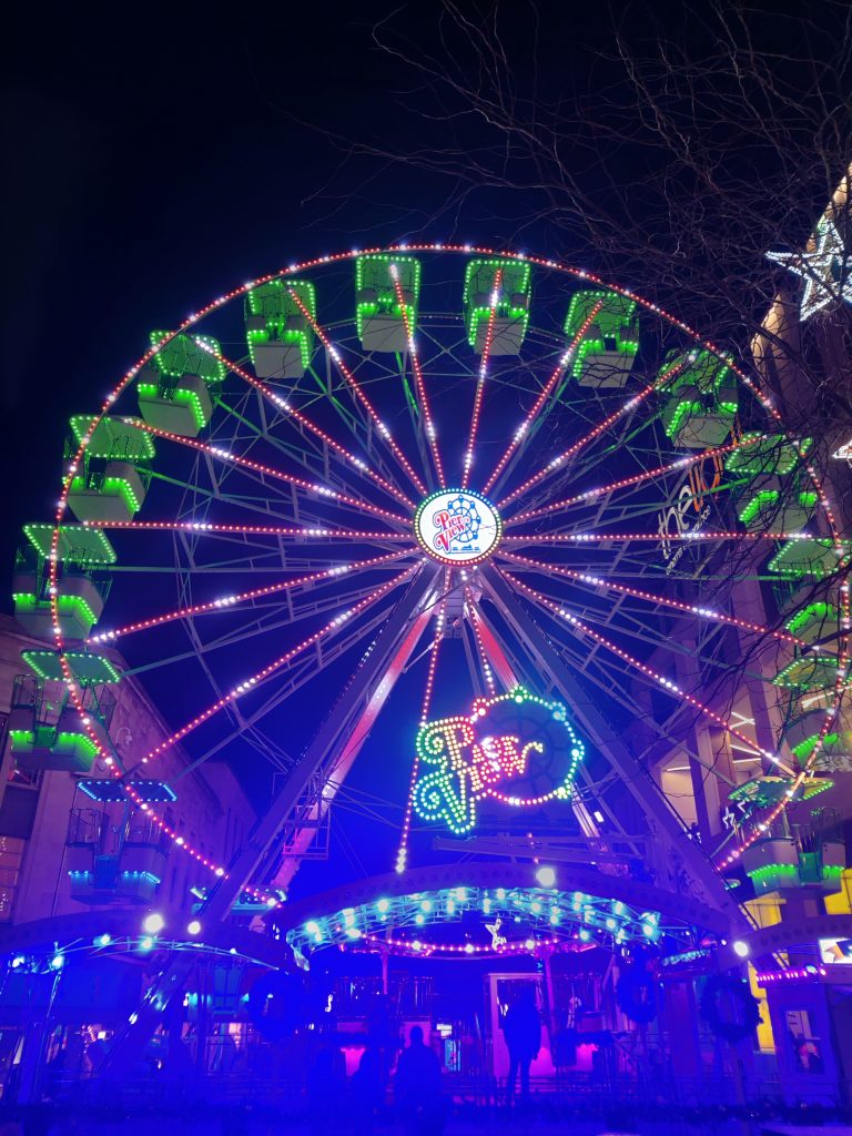 A vibrant giant wheel/ferris wheel illuminated with bright lights against a black sky