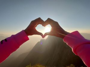 Observing the sunrise through a handcrafted heart shape on a hill's summit.