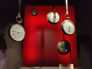 Several pocket watches of varying designs hang against a vibrant red backdrop. 
