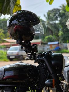 A rider's helmet resting on a motorbike handle under the shade of a tree during a hot day in Kerala, India.