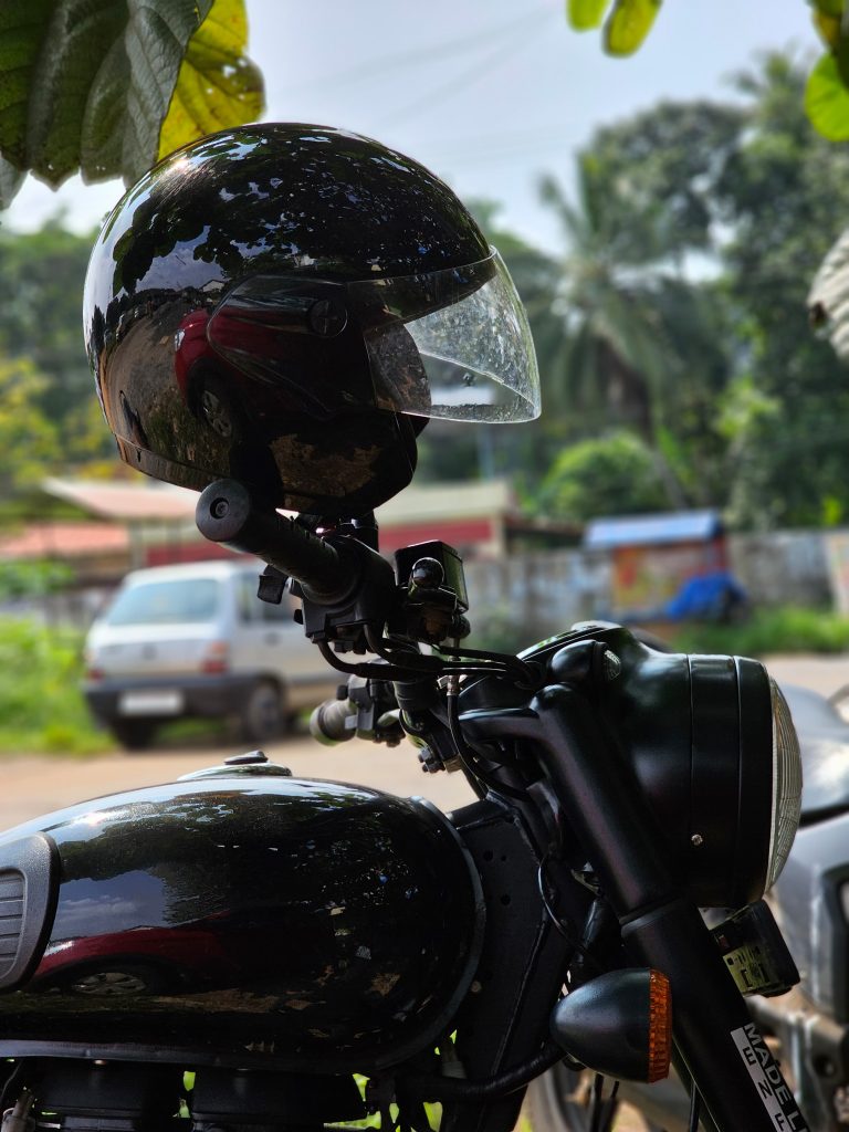 A rider’s helmet resting on a motorbike handle under the shade of a tree during a hot day in Kerala, India.