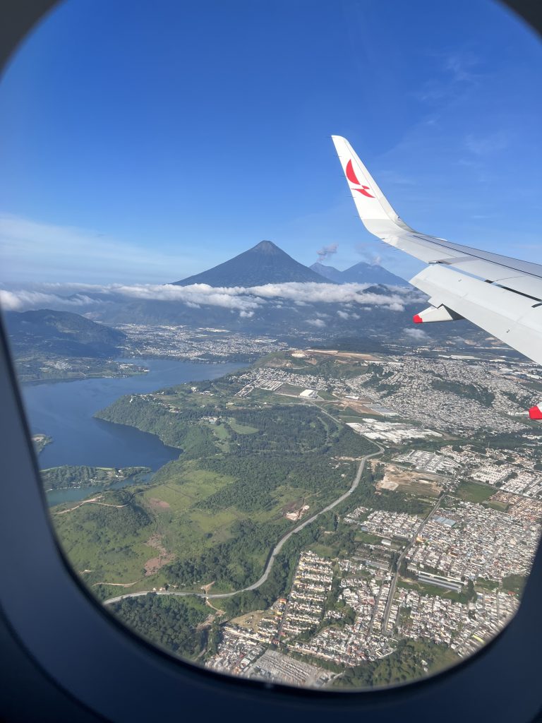 Vista, desde la ventana de un avión, de los volcanes Acatenango, Agua y Fuego de Guatemala. También se observa un lago y los techos de las casas de un poblado.