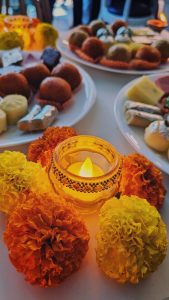 Diwali sweets and flowery decorations using marigold flower placed on a table with a candle in the middle.
