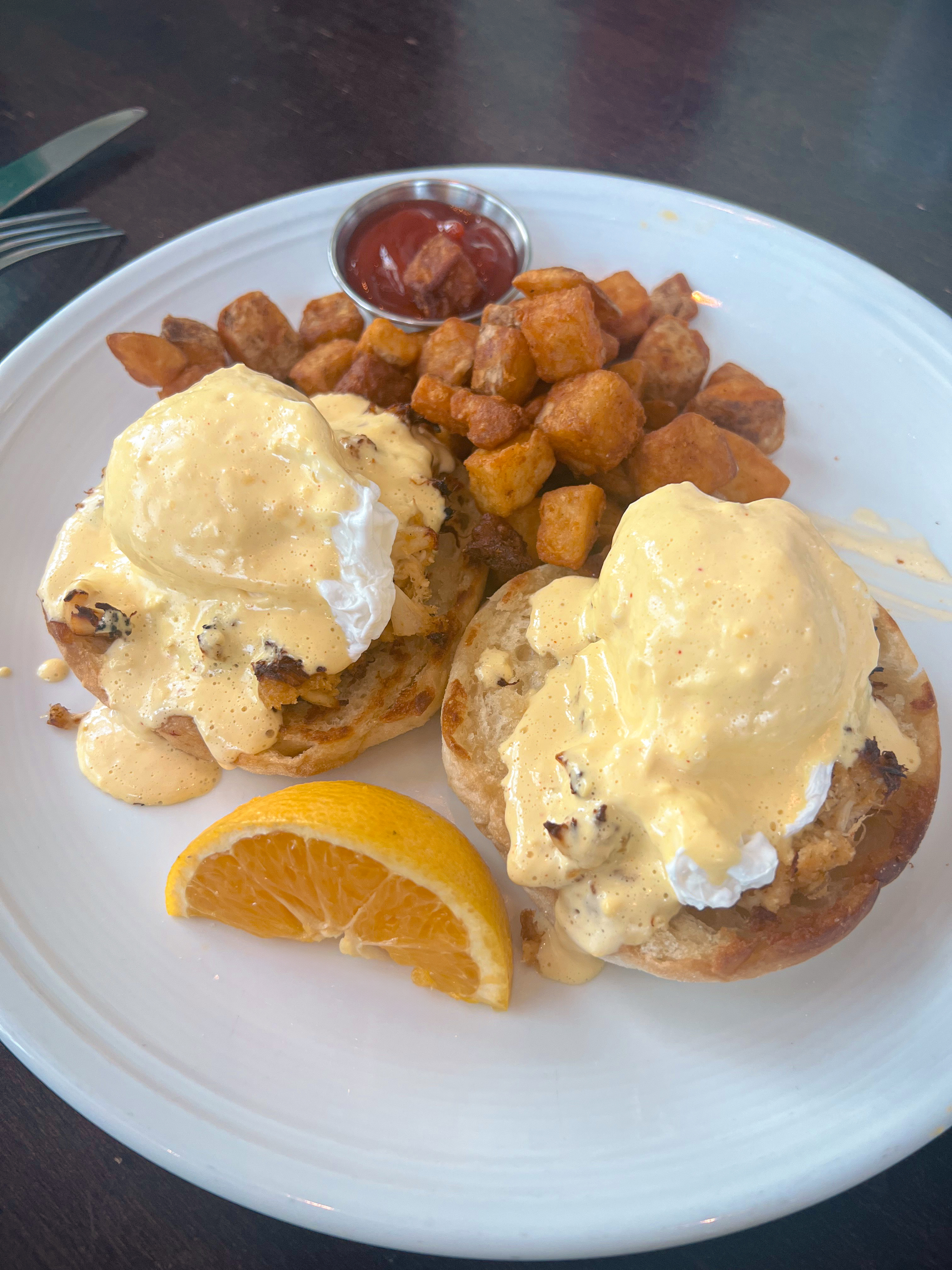 Crab Cakes Benedict breakfast plate with potato wedges and an orange slice