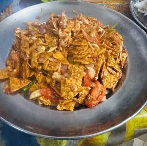 Rimmed silver dish full of food containing meat, tomatoes, peppers, onions in a sauce.