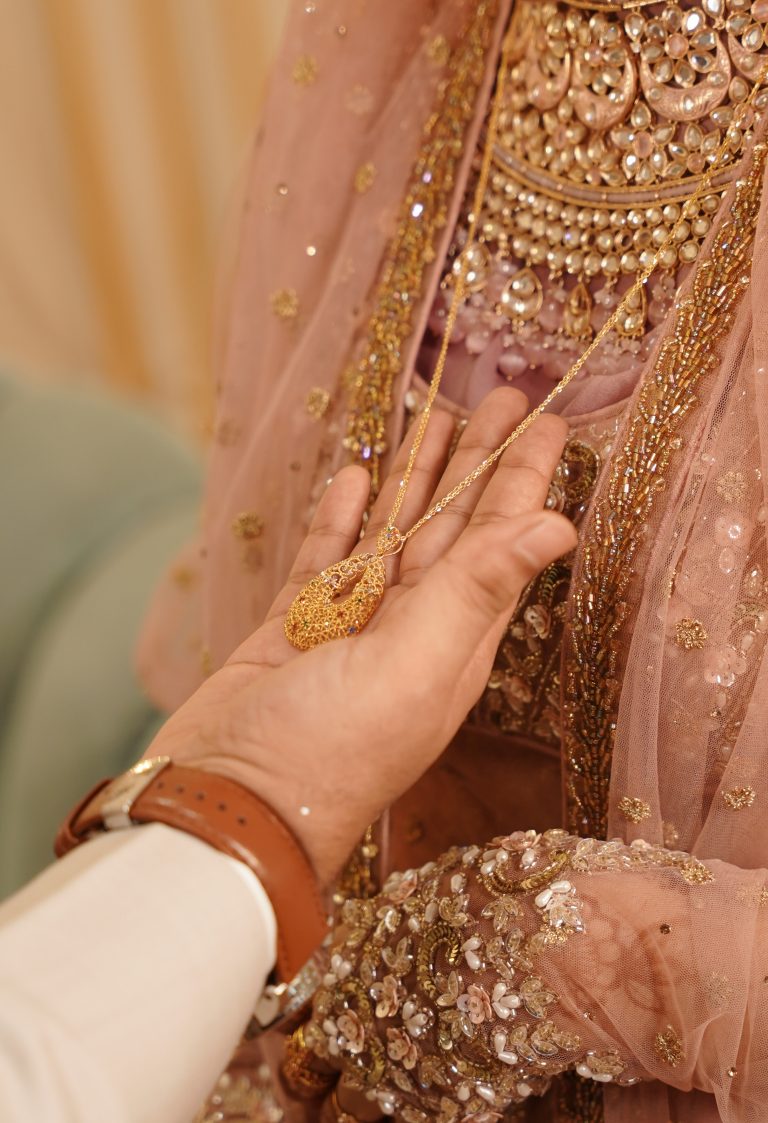 A groom’s hand holding a necklace on a bride.