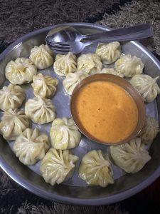 View larger photo: Metal dish filled with Mono dumplings and a side dish of dipping sauce, spoon and fork lay across the edge of the dish.