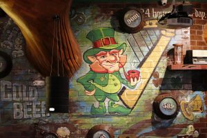 Mural of a leprechaun with a smoking pipe, and vintage décor on a brick wall inside Irish Village bar
