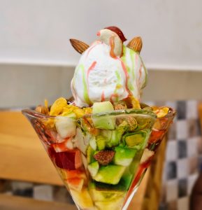 Fruit salad! A scoop of ice cream on top of various cut fruits and nuts. 