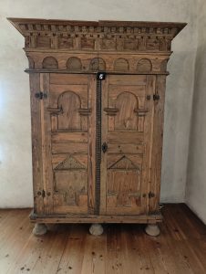 An ornate, vintage wooden cabinet stands against a light-colored wall.