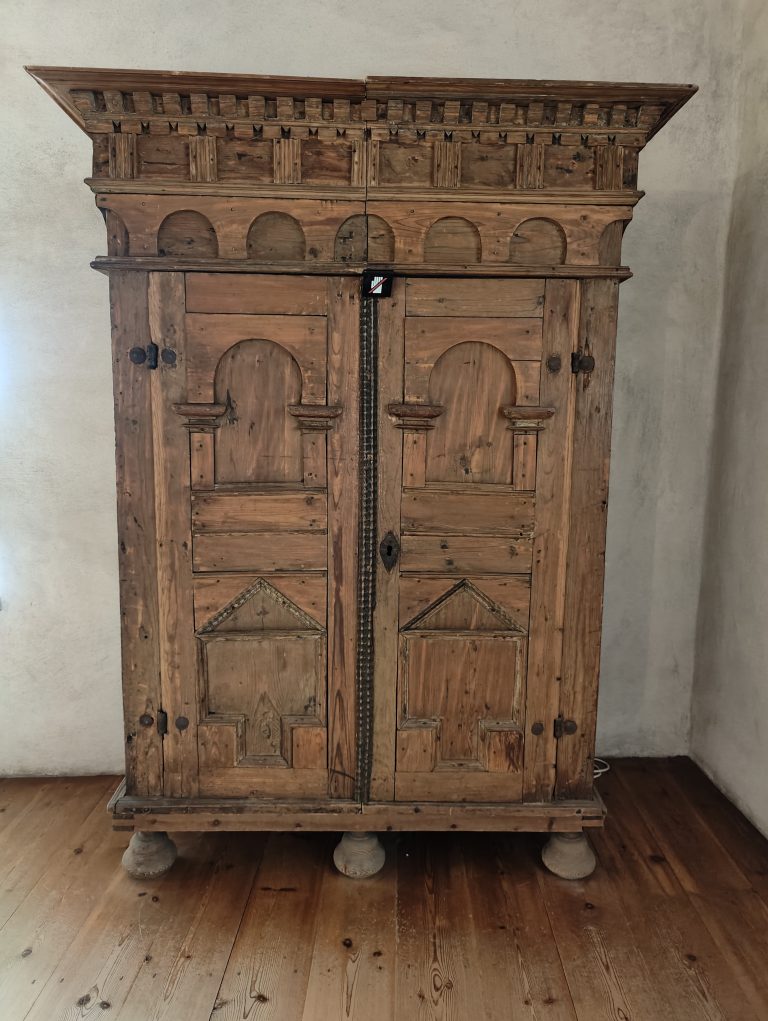 An ornate, vintage wooden cabinet stands against a light-colored wall.