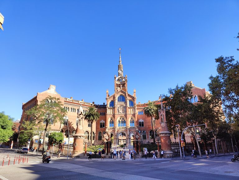 The intricate facade of Hospital de Sant Pau in Barcelona, a stunning example of Catalan Modernisme architecture, with its ornate mosaics and sculptures under a clear blue sky.