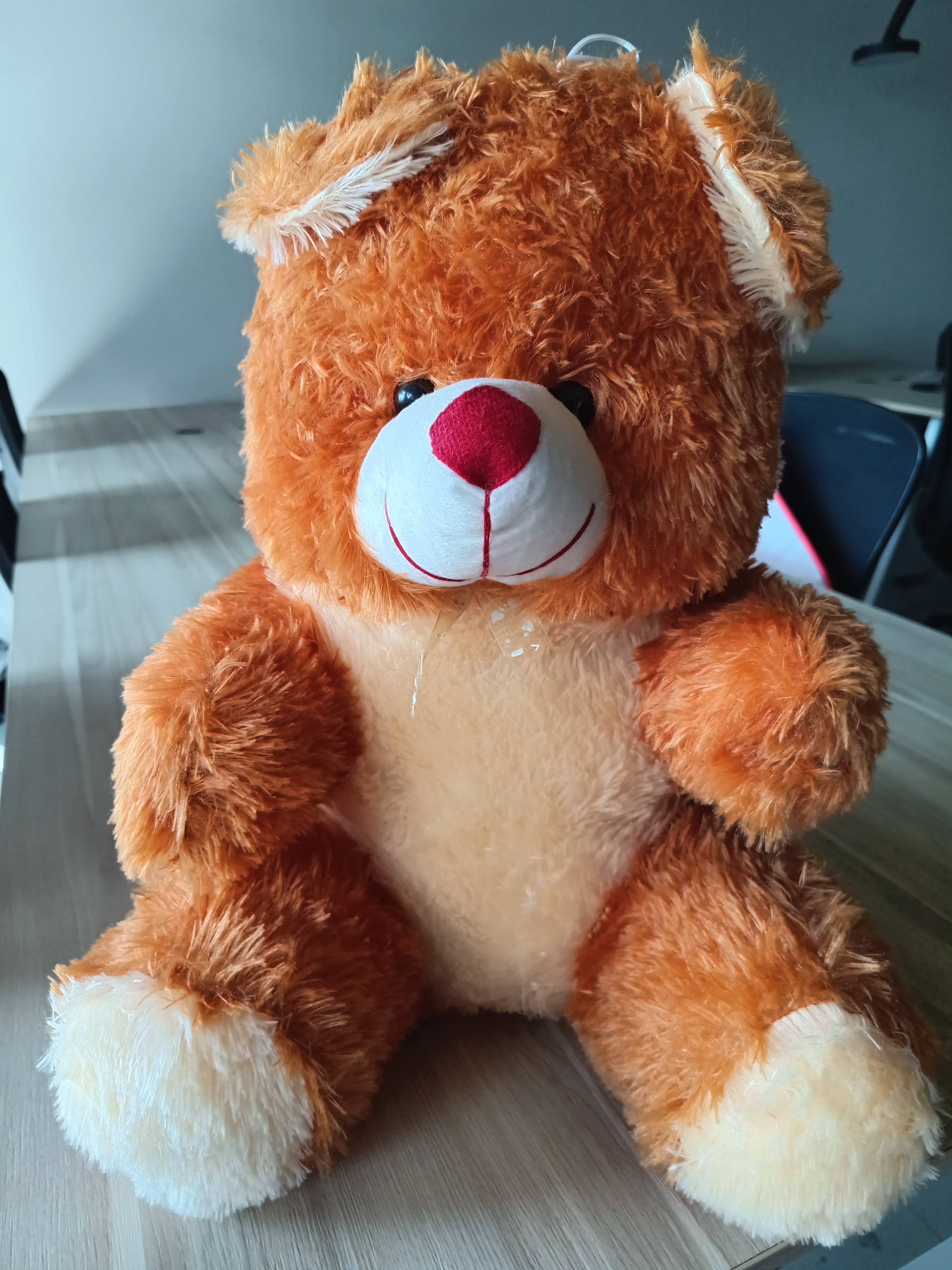 A teddy bear perched on a wooden surface.