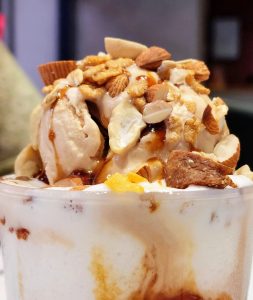 A bowl of ice cream with caramel and nuts toppings. 