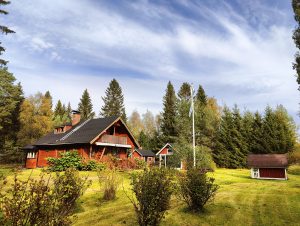 A picturesque wooden cabin with a dark roof sits amid a lush garden. 