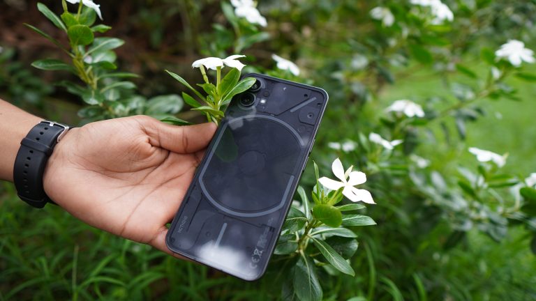 Holding a phone in hand with flowers in the backdrop.