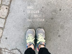 Person wearing running shoes in front of the text “who decides what’s impossible” made with a spray technique on the sidewalk
