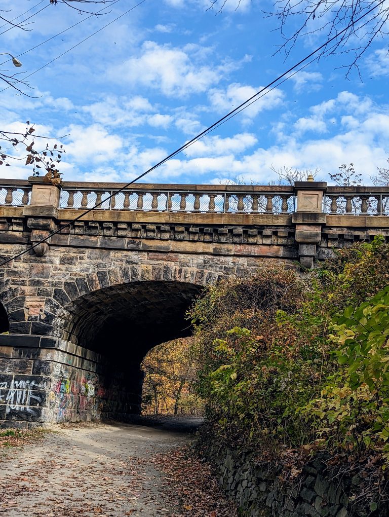 A path running under the arch of a stone bridge with blue sky overhead