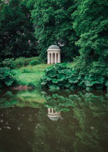  The Lady Alice Temple, Hillsborough Castle, Northern Ireland. A small white temple surrounded by woodland. It’s reflection is visible from the pond just in front of it.
