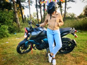 A lady rider with a black helmet, leaning on a motorcycle body toward the camera, looking to her right.