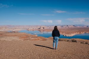 Person standing at a viewpoint, looking out over Lake Powell and the reflection from the rocky formations alongside the lake. 
