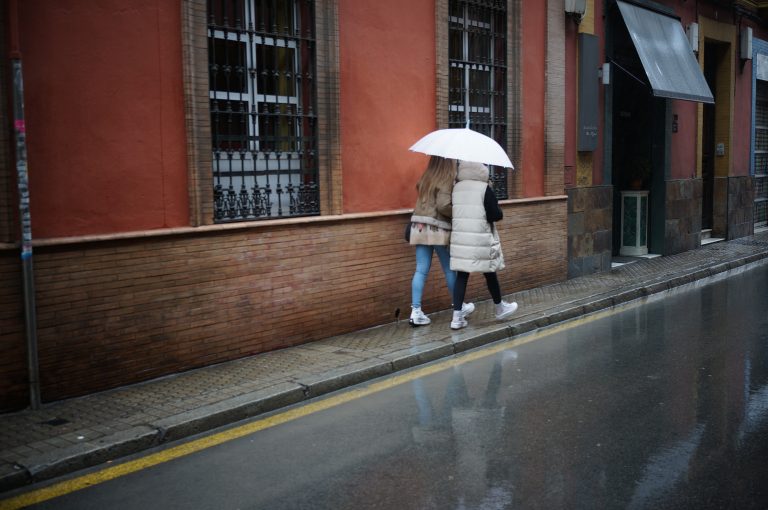 Two women walking under the rain sharing a white umbrella.