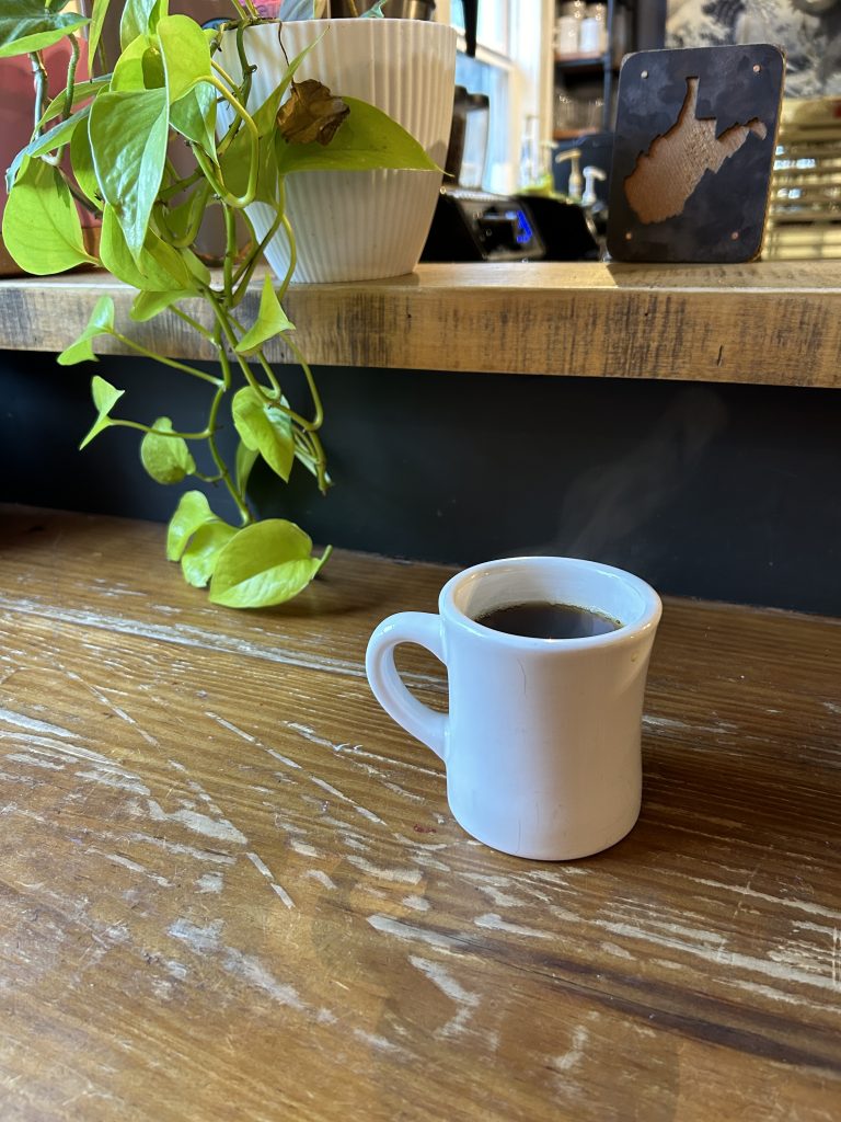 Cup of steaming coffee in white mug and a vibrant money plant on an old wooden counter in Fayetteville, West Virginia.