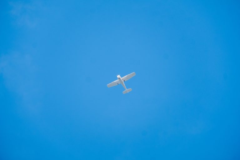 A small white plane photographed from beneath against a clear blue sky.