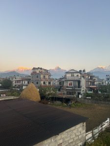 In the foreground, there is a sight of buildings in Pokhara, set against a picturesque backdrop of mountains.
