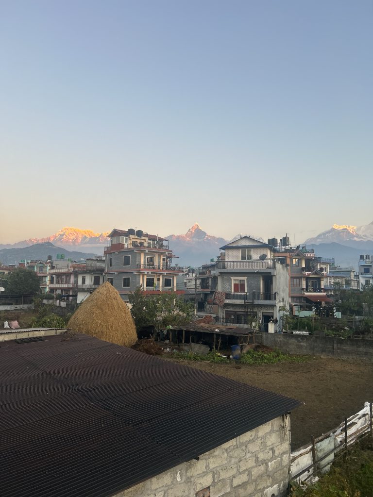 In the foreground, there is a sight of buildings in Pokhara, set against a picturesque backdrop of mountains.