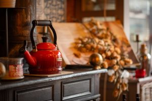 A red kettle on a cupboard with autumn decorations in the background.