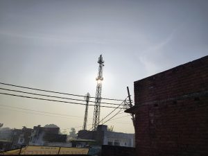 A rooftop photo captures a network tower's silhouette against sunlight, with a textured brick wall for contrast, blending technology, light, and urban architecture visually.