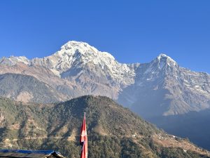 A Nepal flag is in the foreground with the snow-covered Annapurna range in the background.