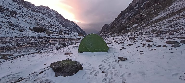 A green tent pitched in snowy mountains.