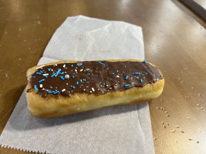 Long narrow doughnut with chocolate on top and blue and silver sprinkles.