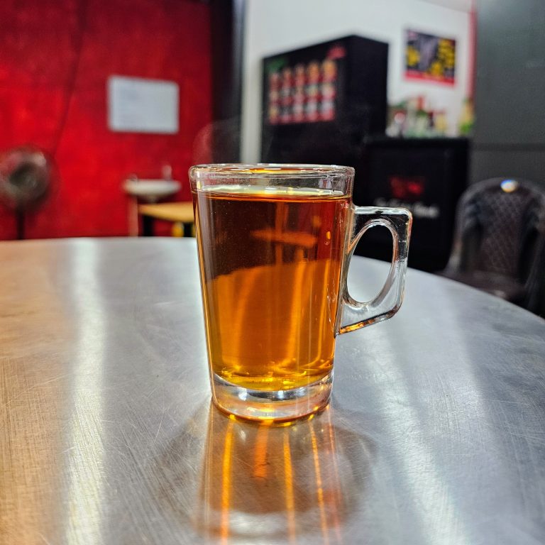 A cup of black tea on a steel table in front of a shop.