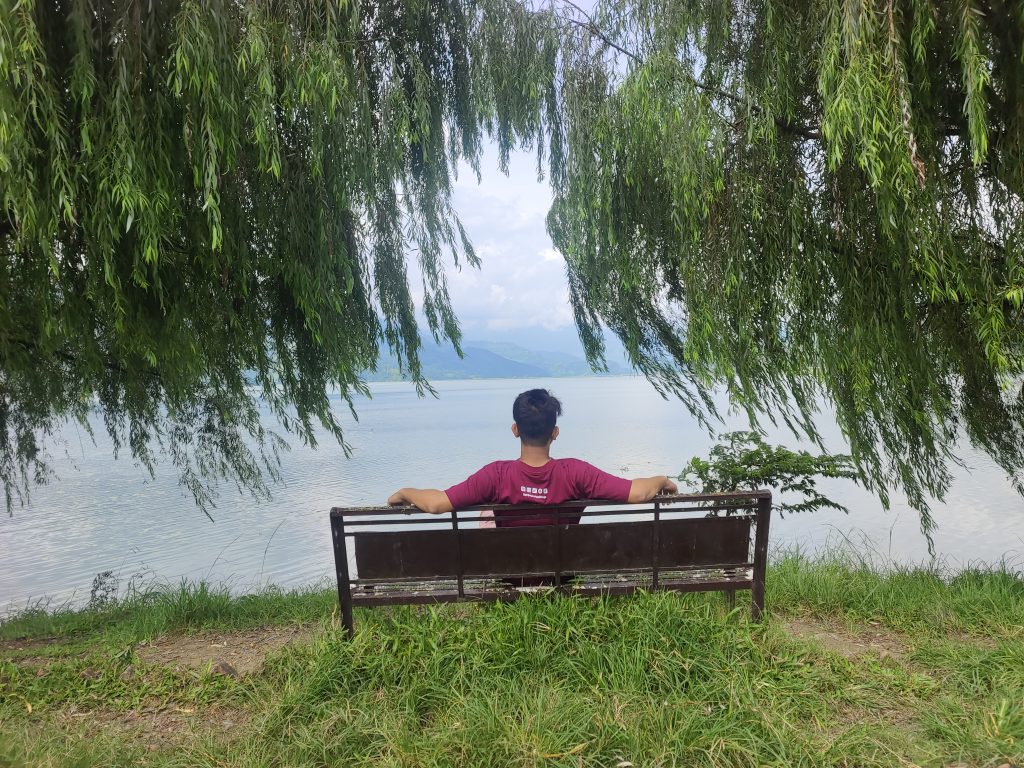 A man sits by Fewa Lake in Pokhara, enjoying the view.