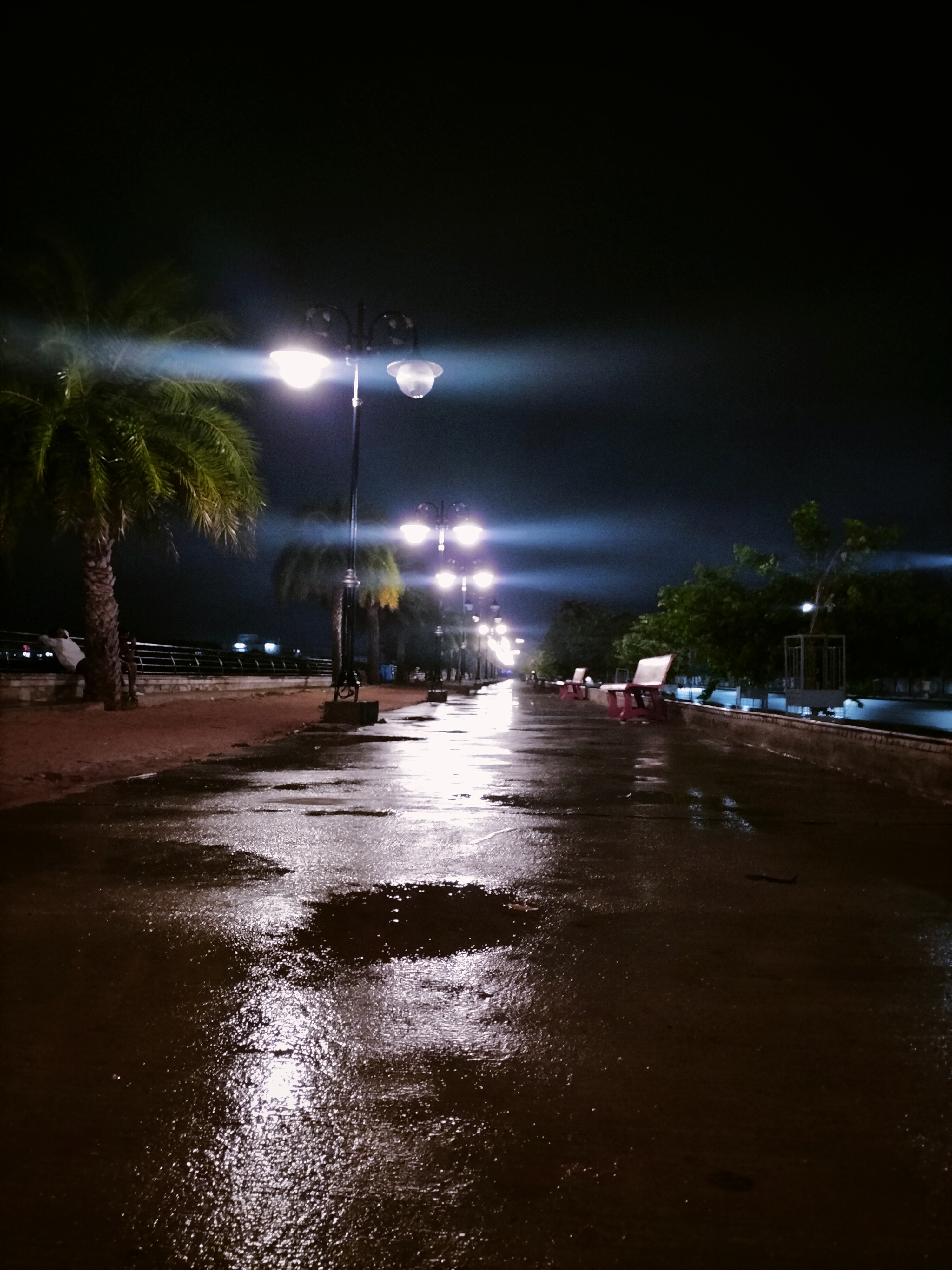 Wet road illuminated by light poles at night, the light is reflecting in the water on the road.