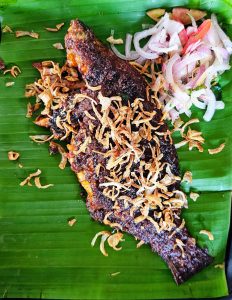 Deep-fried tilapia fish garnished with fried onion served in a banana leaf. 