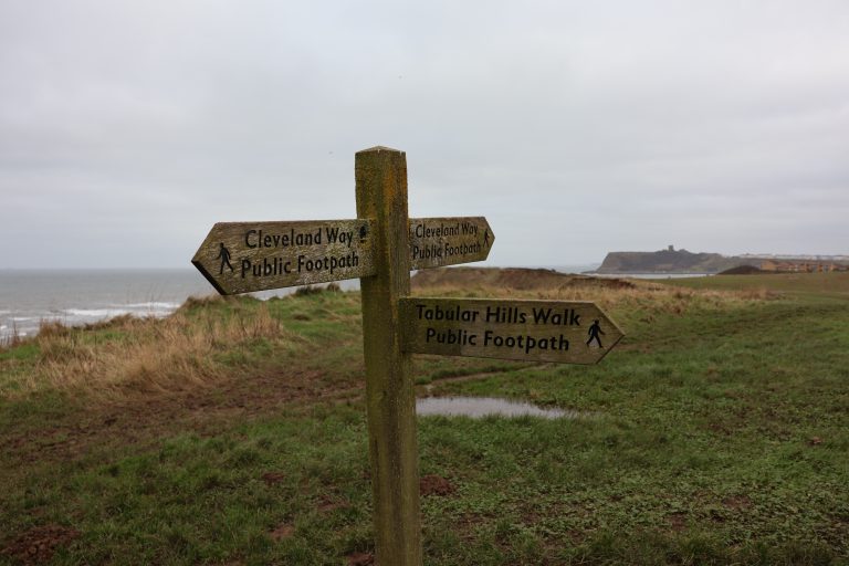 A view over the cliffs of Scarborough. A signpost show the directions for a variety of local walks.