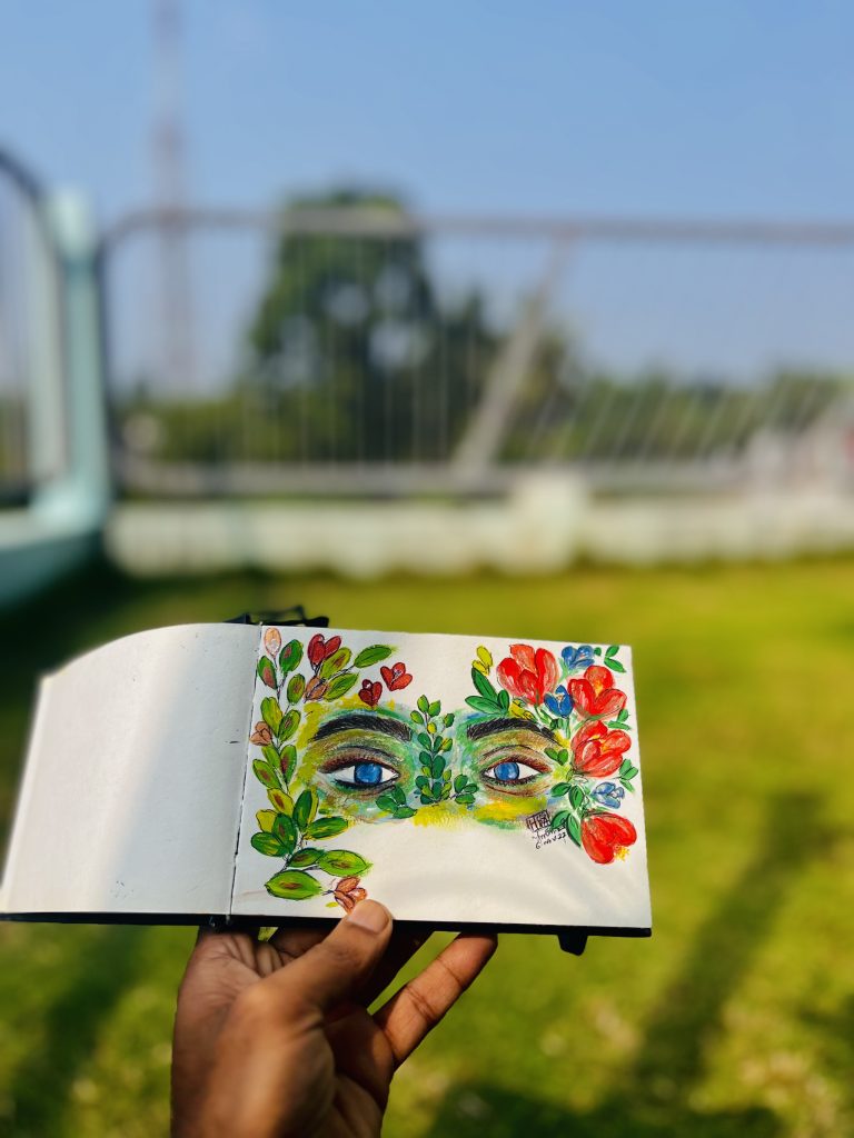 A hand holding a notebook with drawings of eyes along with flowers and leaves.