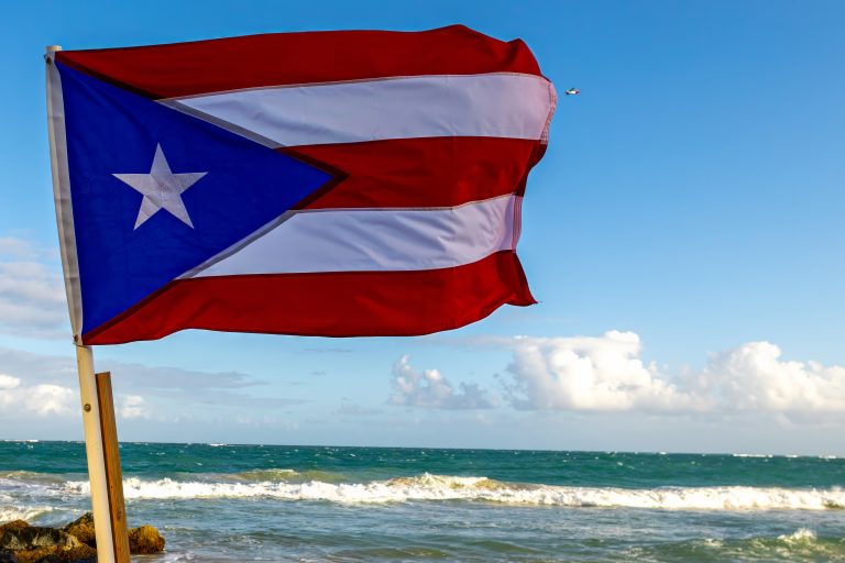 Close up of Puerto Rican flag with a small airplane in the sky and the ocean in the background