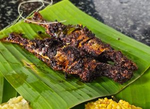A Kerala-style sardine fry, covered with masala, served on a banana leaf with rice and other food.
