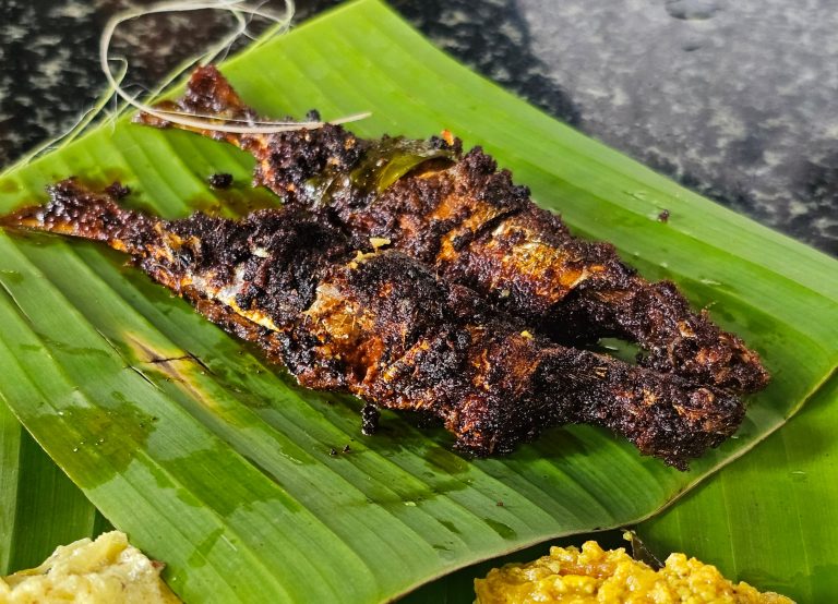 A Kerala-style sardine fry, covered with masala, served on a banana leaf with rice and other food.