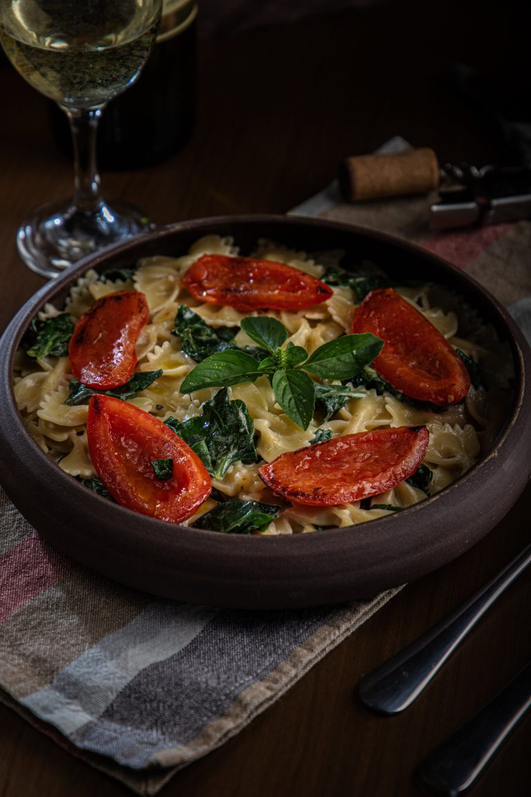 Farfalle with tomatoes and a wine glass next to the plate