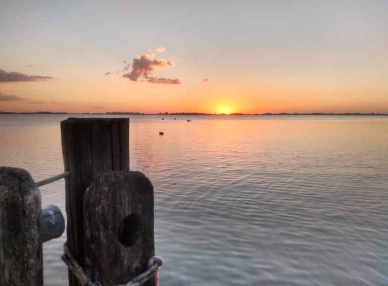 Sunset over a body of water and wooden posts in the foreground. Atardecer laguna Chascomús, Argentina