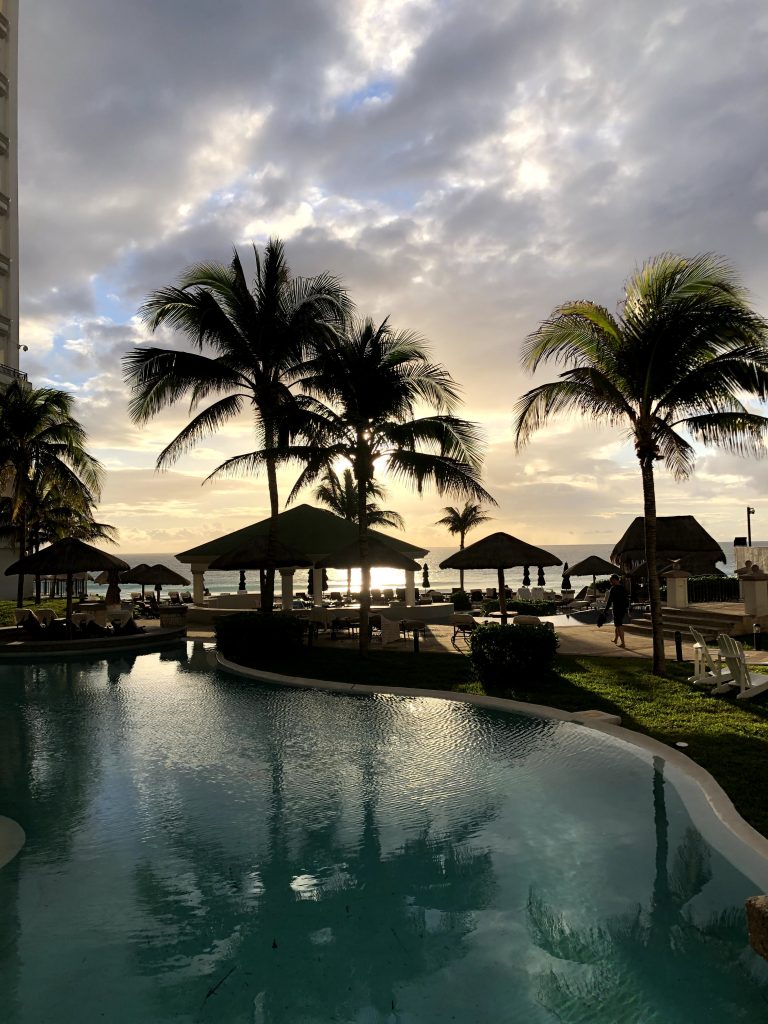 Beachside pool, cabanas, and palm trees at sunset at the JW Marriott Cancun Resort & Spa